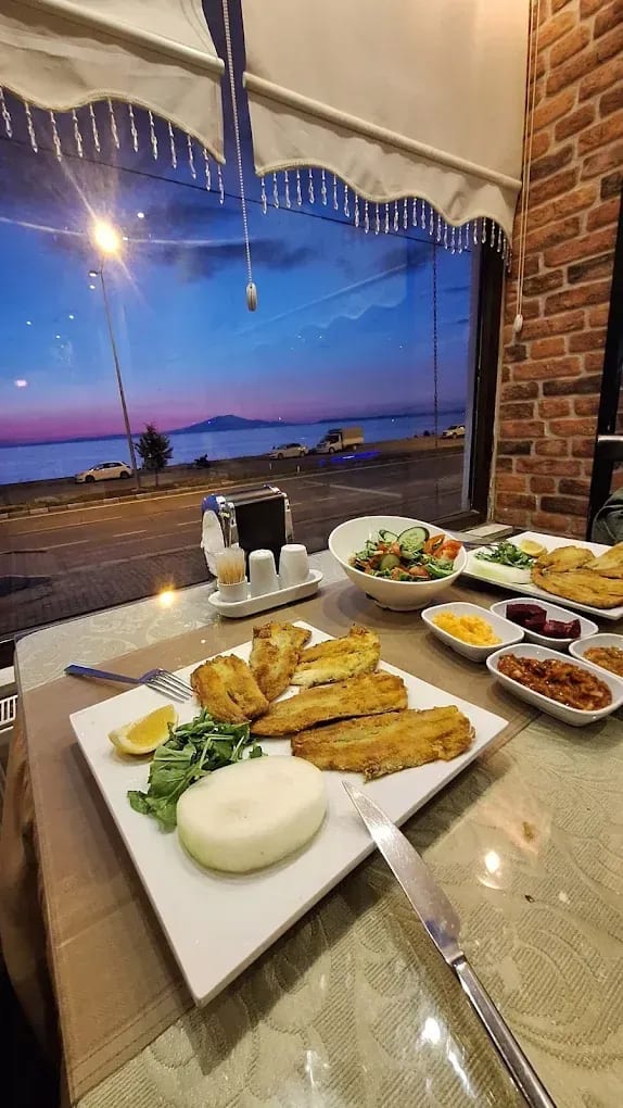 Altınsu salonunda pencere kenarında, göl manzarasına karşı balık ve salata sunumu